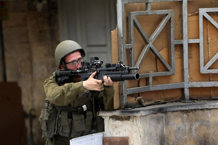 Un soldado israelí aputa su arma contra manifestantes palestinos en la ciudad cisjordana de Hebrón. Foto Xinhua.