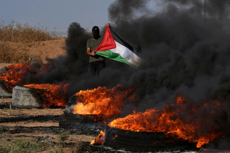 Una persona ondea una bandera de Palestina durante enfrentamientos con las fuerzas israelíes, en la frontera entre Gaza e Israel. Foto Ap