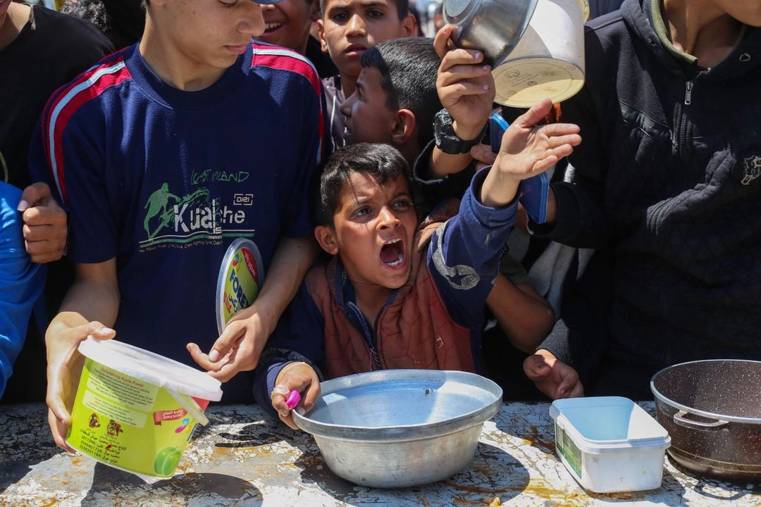 Un niño palestino hace gestos mientras espera una ración de comida caliente distribuida por un comedor social en el campo de refugiados de Nuseirat, en el centro de la Franja de Gaza, el 5 de mayo de 2025.  Foto