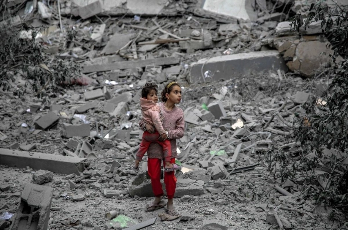 Una niña palestina carga a una niña entre los escombros de las casas destruidas por el bombardeo israelí en la ciudad de Gaza.