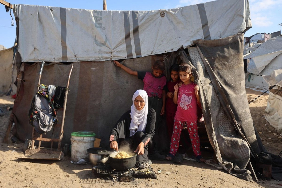 Una mujer palestina cocina junto a niños frente a una tienda de campaña en un sitio para desplazados en Khan Yunis, al sur de la Franja de Gaza, el 29 de septiembre de 2025. 
