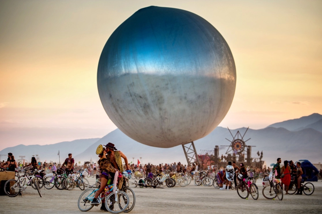 Una pareja que comparte un beso en una bola de discoteca que levita, pieza del colectivo multidisciplinario BIG aka Bjarke Ingels Group, de Copenhague, durante el Burning Man de 2018, festival de música en Nevada, EU, donde no se aceptan comercios ni marcas. Foto cortesía de Bahidorá