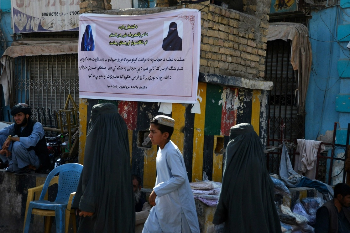 Mujeres con burka pasan junto a un letrero colocado por autoridades talibanas, donde se pide a las mujeres usar hiyab en Kandahar, el 16 de junio de 2022. Foto Afp 