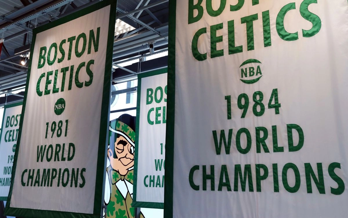 Lucky the Leprechaun, el logo de los Boston Celtics, se asoma entre las pancartas del campeonato de los Celtics colgadas en las nuevas instalaciones de entrenamiento de su equipo de baloncesto, el martes 19 de junio de 2018, en Boston. Foto