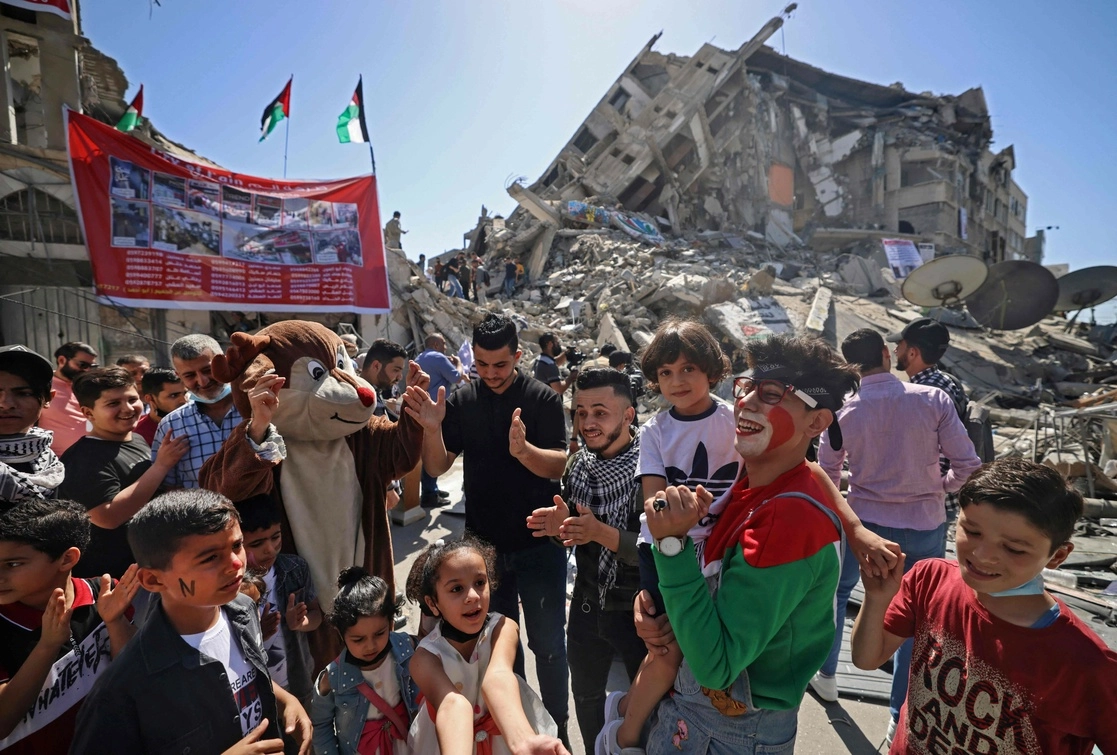 Palestinos entretienen a sus niños con una botarga frente a los escombros de la torre al-Shourouk, destruida recientemente por bombardeos israelíes en Gaza. Foto Afp