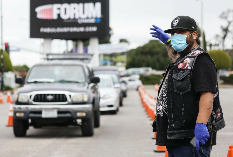 Un voluntario dirige el tráfico mientras usa una máscara facial en una distribución de comestibles gratuita en cumplimiento del Viernes Santo para aquellos afectados por la pandemia de coronavirus, en Inglewood, California. Foto AFP