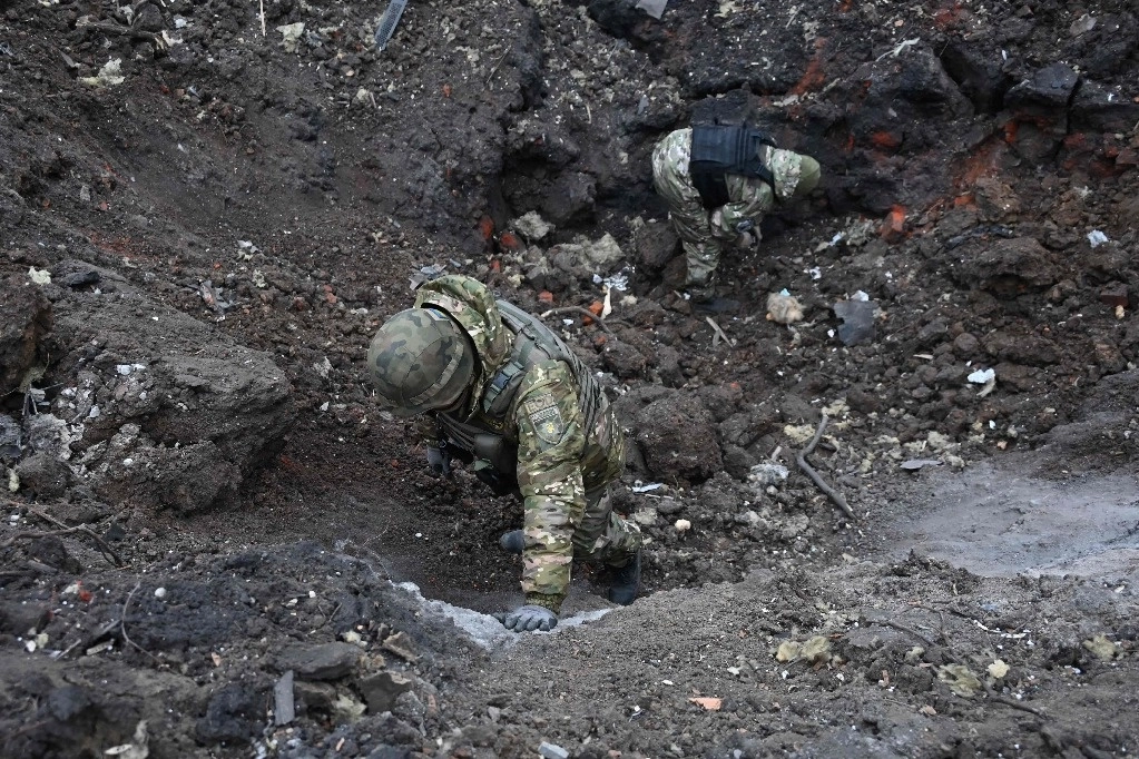 Miembros del Servicio de Eliminación de Explosivos de Ucrania (EOD) examinan un cráter fuera de un edificio residencial dañado en el centro de Kharkiv después de un ataque con misiles el 2 de enero de 2024. Foto Afp
