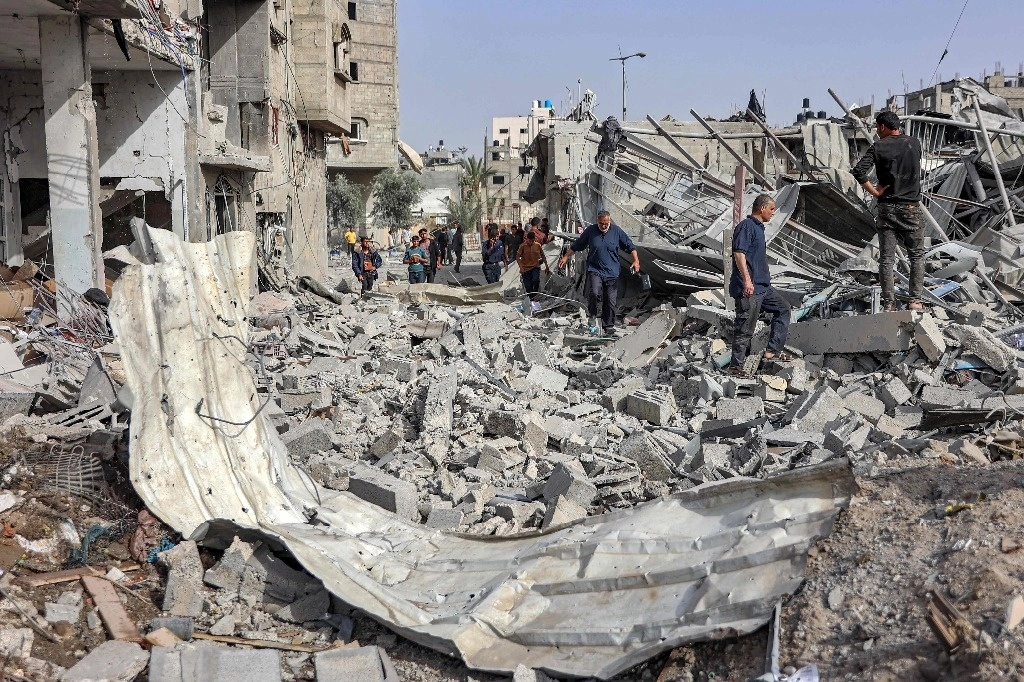 Personas caminan entre los escombros de un edificio colapsado, tras el bombardeo israeló en Gaza. Foto Afp 