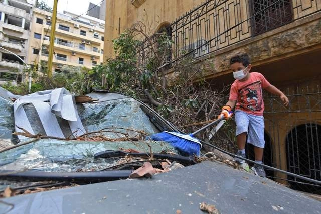 Un niño libanés limpia un auto dañado por las explosiones en Beirut. Foto Afp 