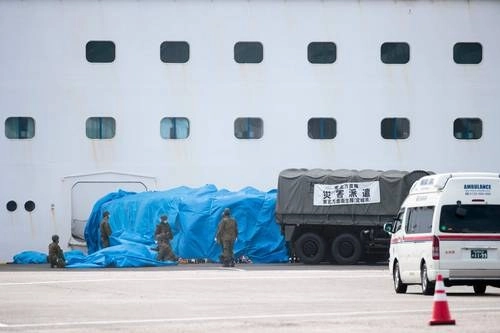 Elementos de la fuerza de autodefensa de Japón colocan un vehículo militar en una puerta del crucero 'Diamond Princess', con alrededor de 3 mil 600 personas en cuarentena a bordo, donde ayer se reportaron 218 contagios, en la terminal de Daikaku Pier, en el puerto de Yokohama. Foto Afp