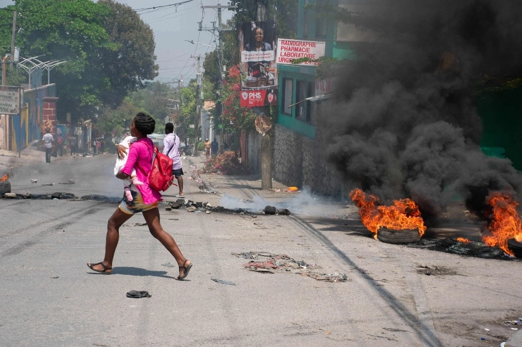 Una mujer con su bebé en brazos huye corriendo de un sitio donde ocurrieron ayer tiroteos en Puerto Príncipe, Haití. Foto Afp 