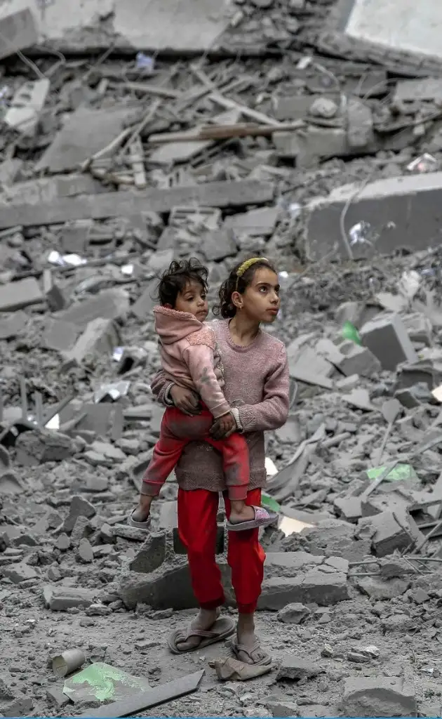 Una niña lleva en brazos a un pequeño entre las ruinas de edificios en Gaza. La creciente crisis de alimentos en la franja ha causado una catástrofe en la inmensa mayoría de la población palestina, reiteró ayer la Oficina de Coordinación de Asuntos Humanitarios de la ONU. “Una vez que se declara la hambruna es demasiado tarde para mucha gente”, alertó. Foto Afp 