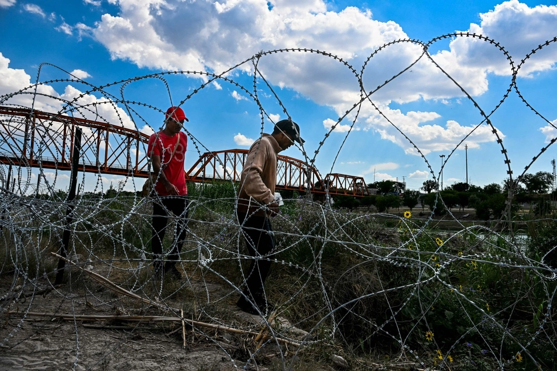 Migrantes que cruzaron ilegalmente el Río Grande caminan a lo largo de una alambrada en Eagle Pass, Texas, cerca de la frontera con México. Foto Afp