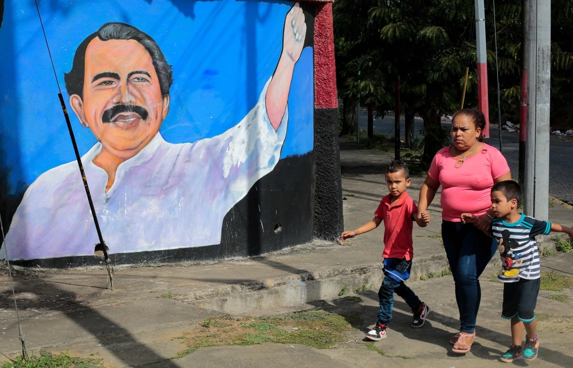 Una mujer y dos niños pasan junto a un mural del presidente nicaragüense, Daniel Ortega, en Managua, el 10 de enero de 2022. Foto Afp