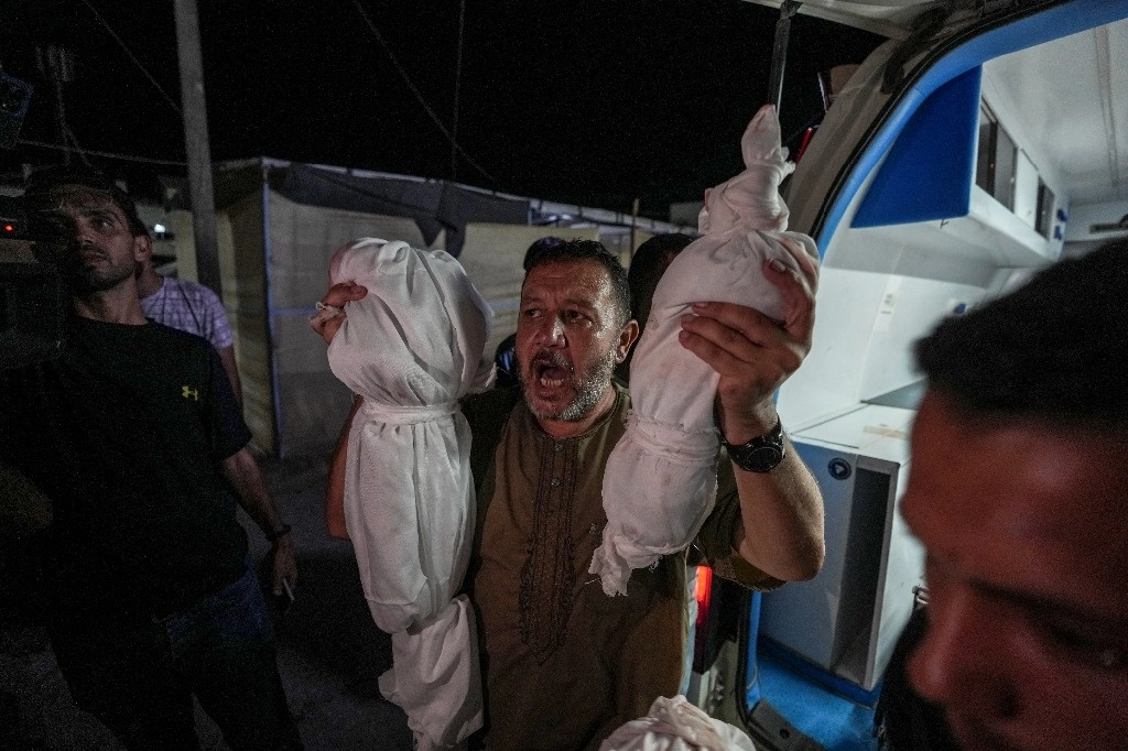 En la morgue del hospital en Deir al Balah, el palestino Osama al Taweel reprocha la incursión israelí en Gaza mientras sostiene los cuerpos de sus nietos víctimas de un reciente ataque aéreo. Foto Ap