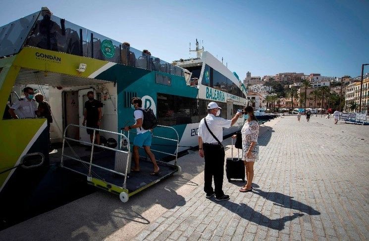 Un empleado toma la temperatura de un pasajero antes de abordar un ferry en el puerto de Ibiza. Foto Afp