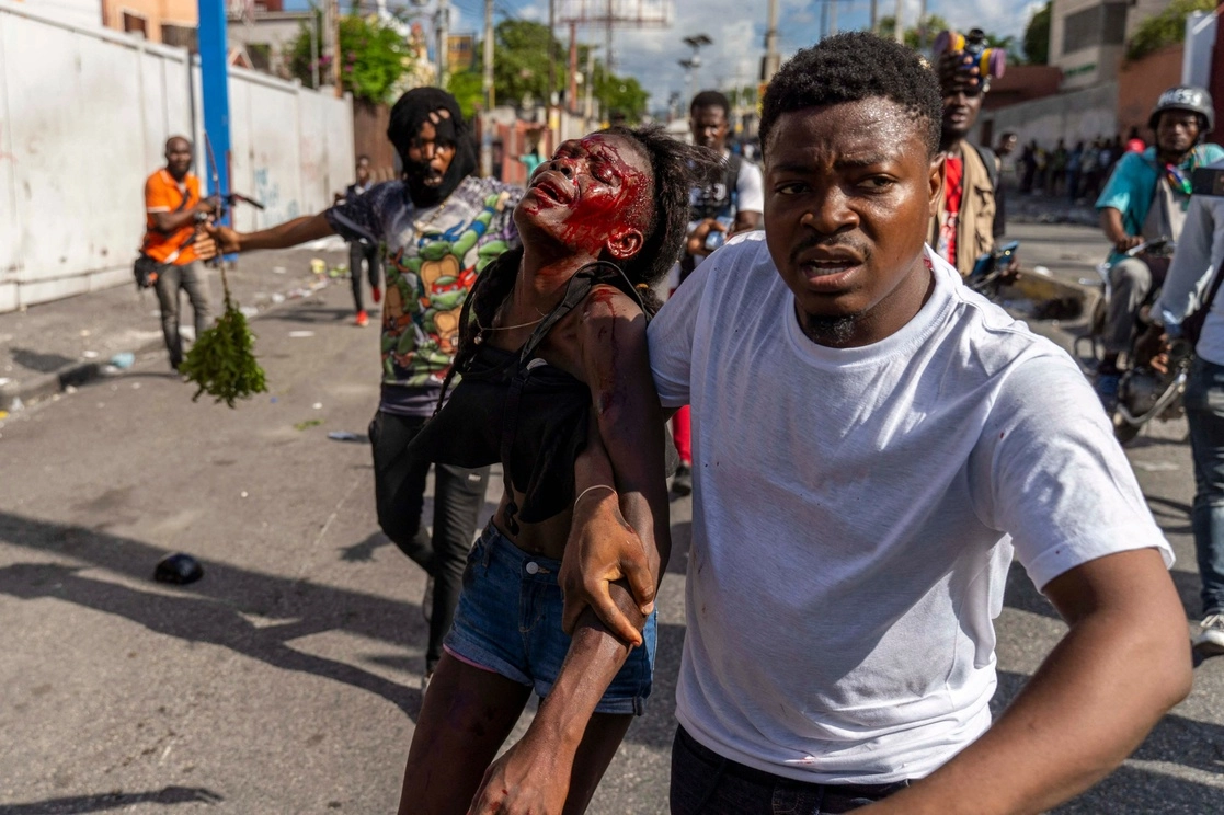 Personas ayudan a una mujer herida durante una protesta en Haití. Foto Afp