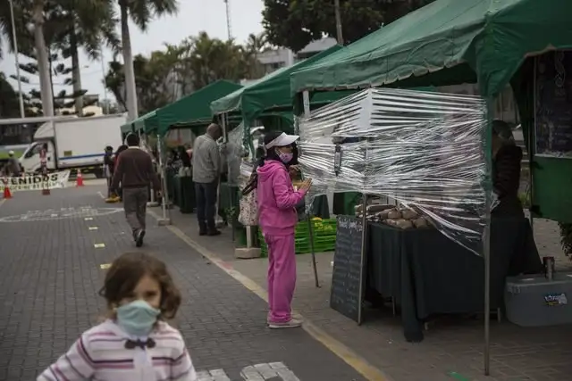 Una mujer habla con un vendedor en un tianguis a través de un plástico protector en el vecindario de Barranco, en Lima, Perú. Foto Ap