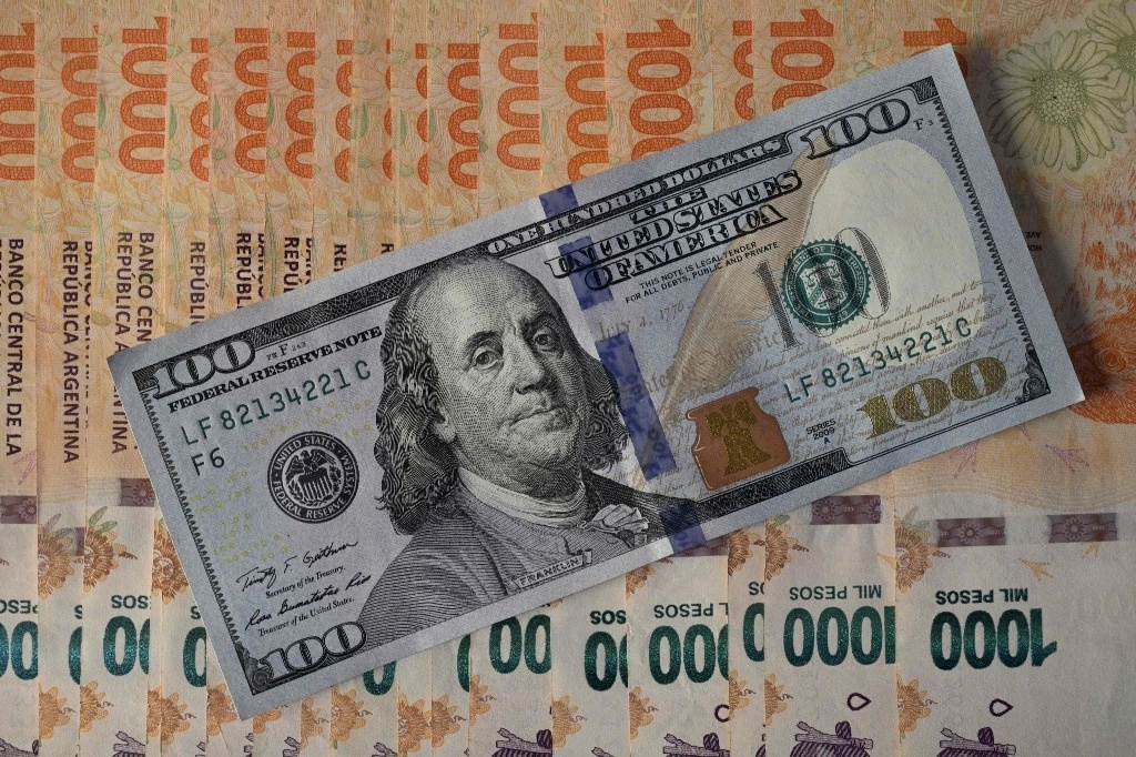 Esta foto ilustrativa muestra billetes de 1.000 pesos argentinos debajo de un billete de 100 dólares en Buenos Aires el 9 de agosto de 2022. Foto Afp/ Archivo 