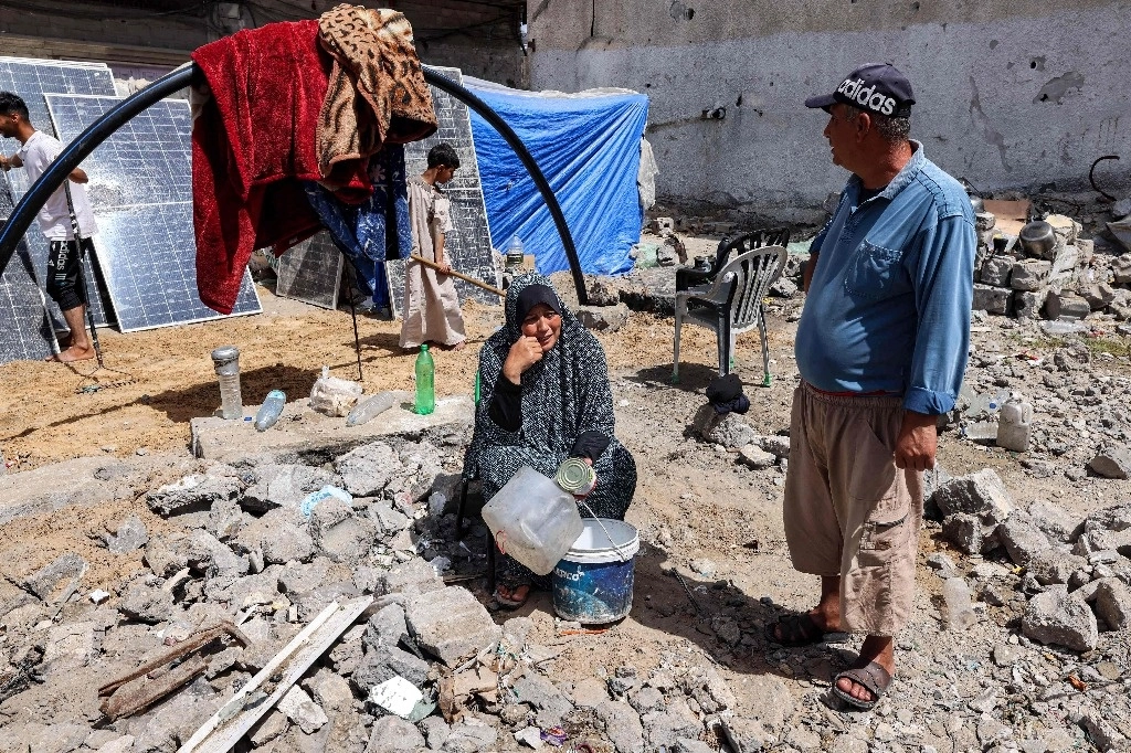 Una mujer sentada sosteniendo contenedores vacíos afuera de una tienda de campaña levantada junto a un edificio destruido en Rafah, en el sur de la Franja de Gaza, el 5 de abril de 2024, en medio del conflicto en curso en el territorio palestino entre Israel y el grupo militante Hamas. Foto AFP 