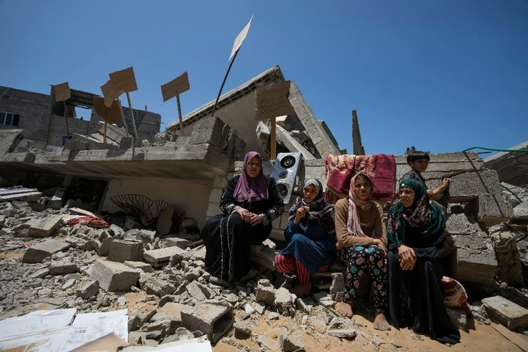 Los miembros de la familia Nabhan, se sientan frente a las ruinas de su hogar, que fue destruido en un ataque aéreo israelí en Jabaliya, al norte de la Franja de Gaza, el domingo 14 de mayo de 2023. Foto Ap