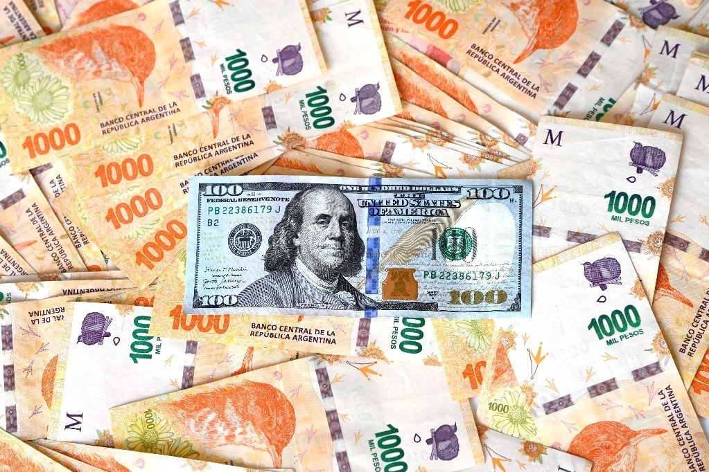 Esta ilustración muestra un billete de 100 dólares encima de pesos argentinos. Foto Afp