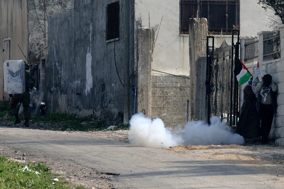 Palestinos que ondean una bandera nacional se cubren el rostro de los gases lacrimógenos durante los enfrentamientos con tropas israelíes tras una protesta contra la expropiación de tierras palestinas por parte de Israel en la Cisjordania ocupada, en la aldea de Kfar Qaddum, cerca del asentamiento judío de Kedumim, el 17 de febrero de 2023. Foto Afp