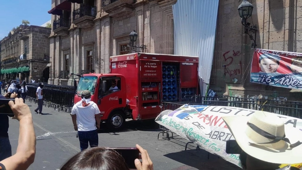 Encapuchados secuestraron ayer un camión de una empresa refresquera, con el que intentaron derribar las puertas del palacio de gobierno, en Morelia, Michoacán. También causaron destrozos y grafitearon edificios de la administración estatal, así como automóviles particulares y oficiales. Foto 'La Jornada'