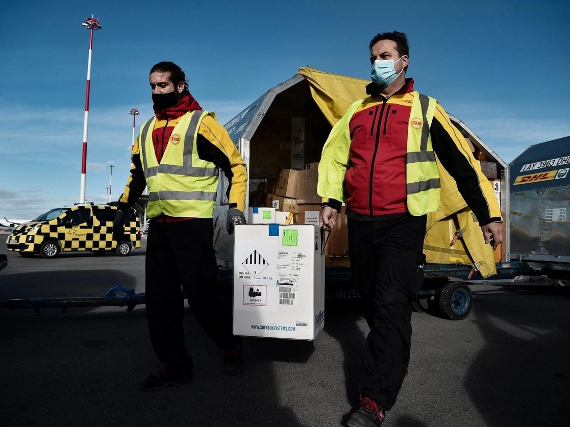 Trabajadores del Aeropuerto Internacional de Macedonia transportan cajas que contienen la vacuna Pfizer-BioNTech contra Covid-19, en Grecia, mientras el país se prepara para comenzar su campaña nacional de vacunación, el 29 de diciembre de 2020. Foto Afp 