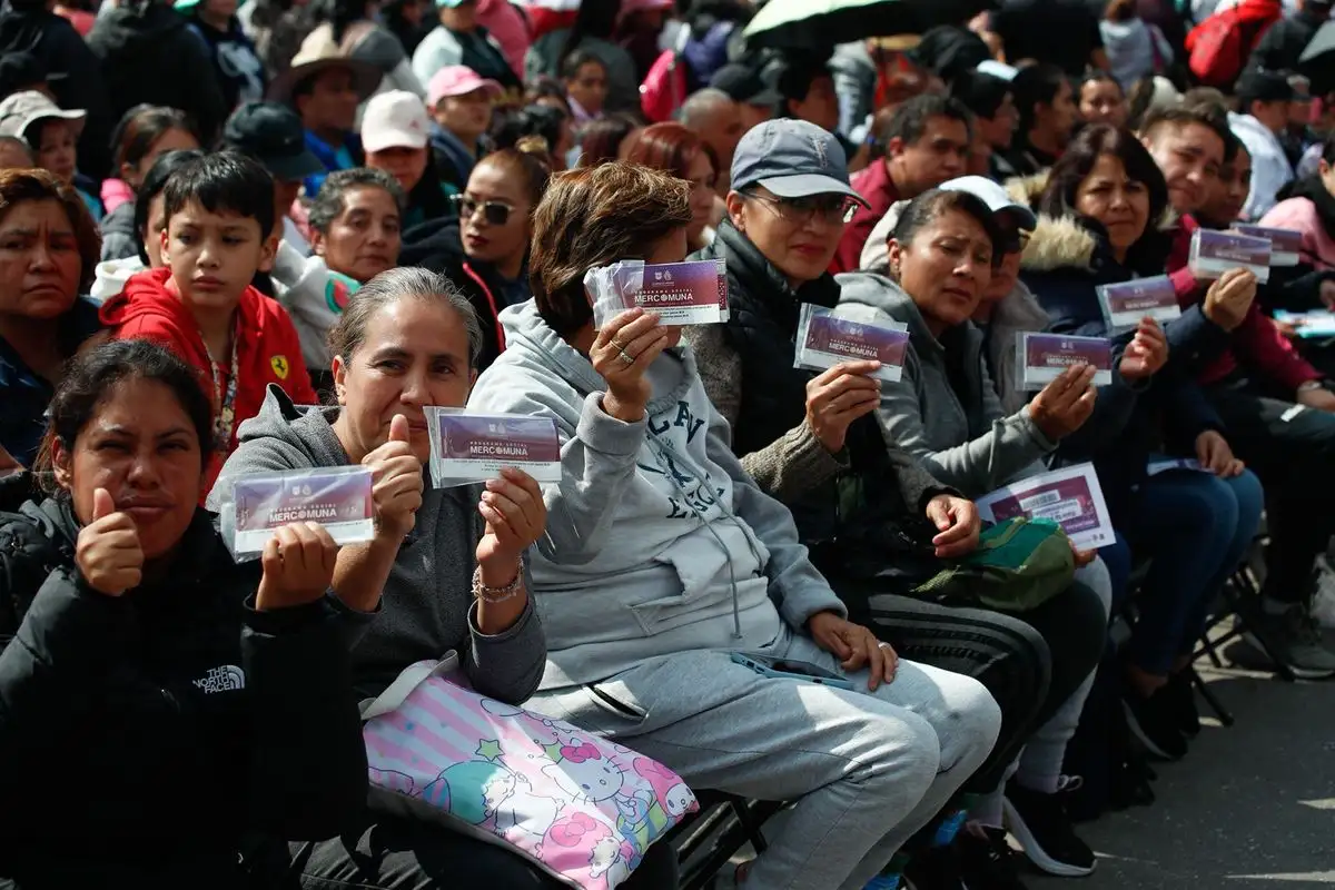 Personas asisten al evento donde la jefa de gobierno de la CDMX, Clara Brugada, encabeza la entrega del programa "Mercomuna", en el Zócalo capitalino, el 26 de agosto de 2025.