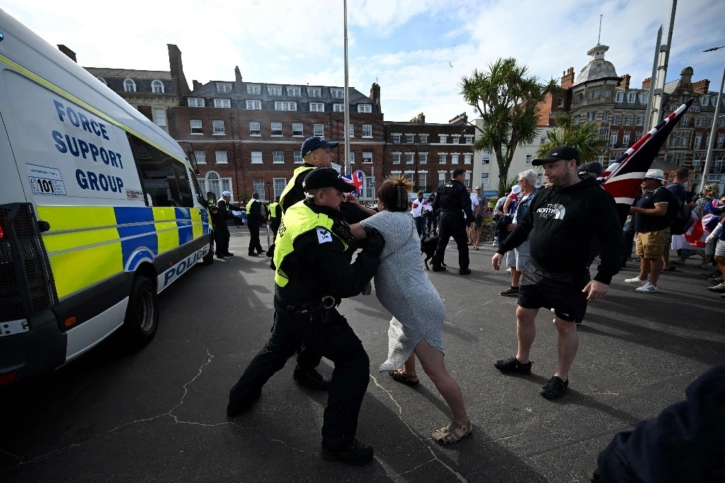 Policía retiene a una mujer que participa en una manifestación convocada por la extrema derecha en Weymouth, Inglaterra. Foto Afp