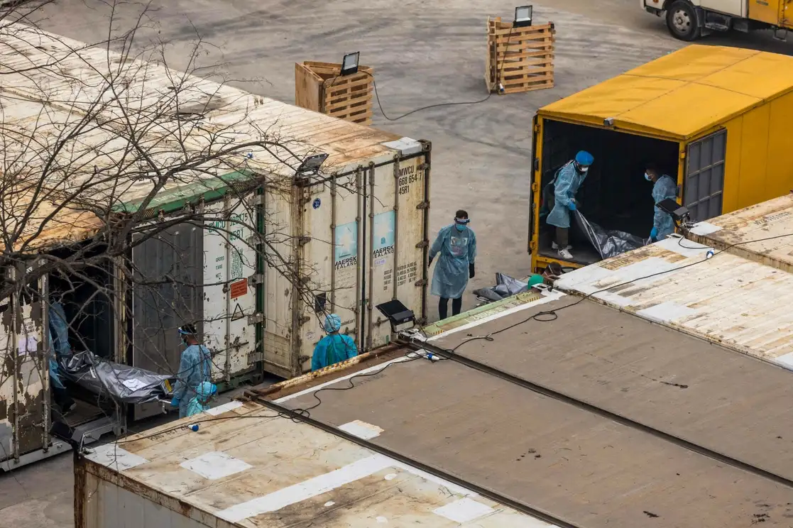 Trabajadores trasladan los cuerpos de personas fallecidas por covid-19 de un camión a un contenedor refrigerado en el depósito de cadáveres público de Fu Shan en Hong Kong, en medio del peor brote de coronavirus de la historia de la ciudad que provocó que hospitales y morgues estén desbordados y que se expanda el sistema de campamentos de cuarentena, el 16 de marzo de 2022. Foto Afp