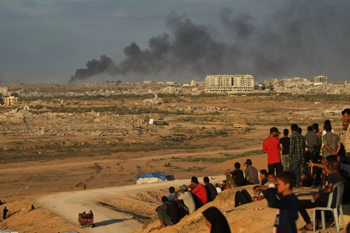 Palestinos desplazados a un lado de la carretera costera cerca de Wadi Gaza observan a lo lejos el humo causado por ataques israelíes, el 9 de octubre de 2025. Foto