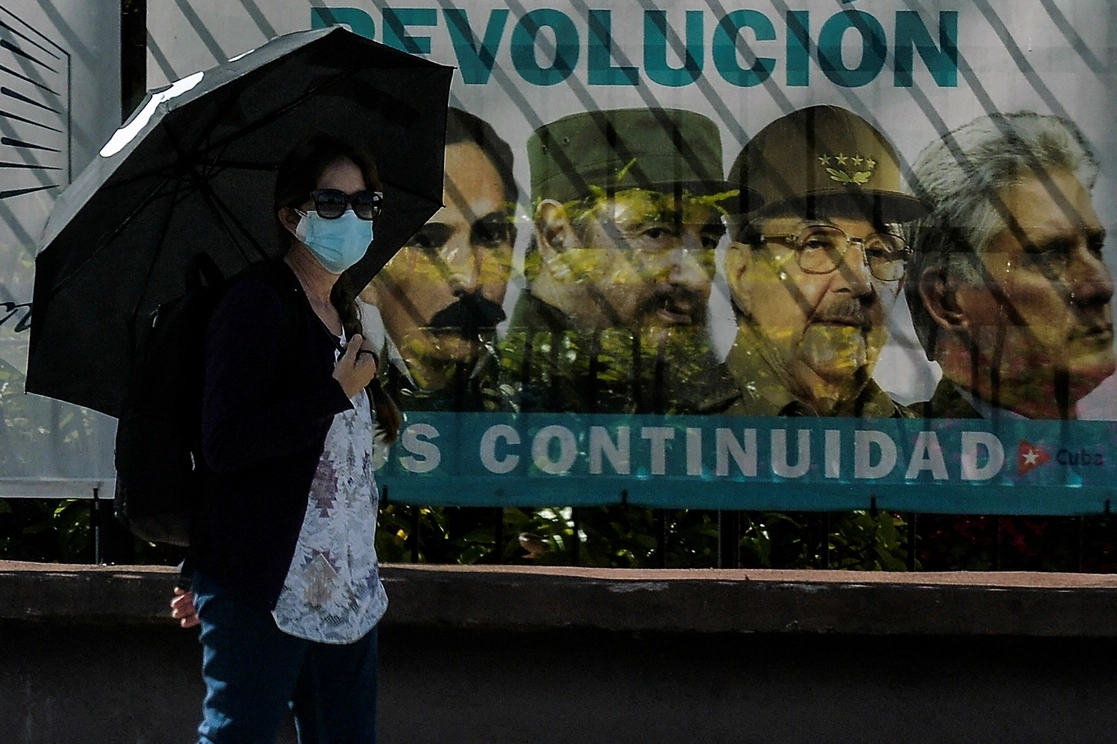 Una mujer, con cubrebocas, camina cerca de un cartel que tiene las imágenes de José Martí, y los hermanos Castro, Fidel y Raúl, así como del actual presidente cubano Miguel Díaz-Canel, en La Habana, Cuba, el 3 de junio de 2021. Foto Afp