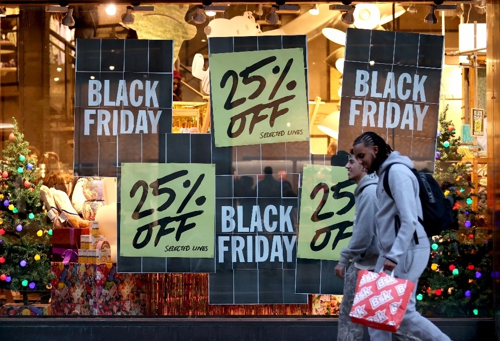 Personas caminando frente a un escaparate que muestra carteles de rebajas del "Black Friday". Foto Xinhua