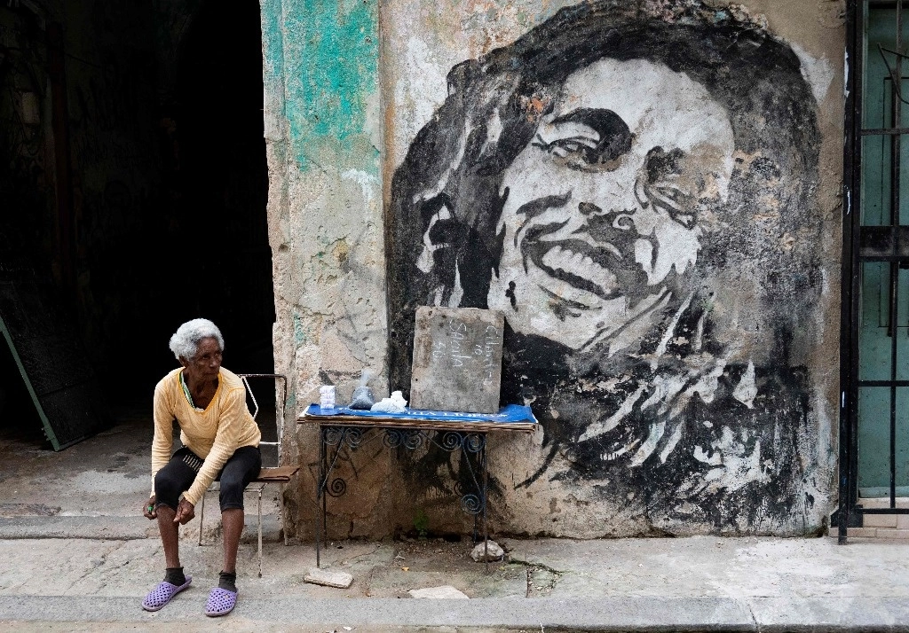 Una anciana vende frijoles y cigarrillos junto a un mural que representa al cantante jamaicano Bob Marley en una calle de La Habana, 30 enero 2024. Foto Afp.
