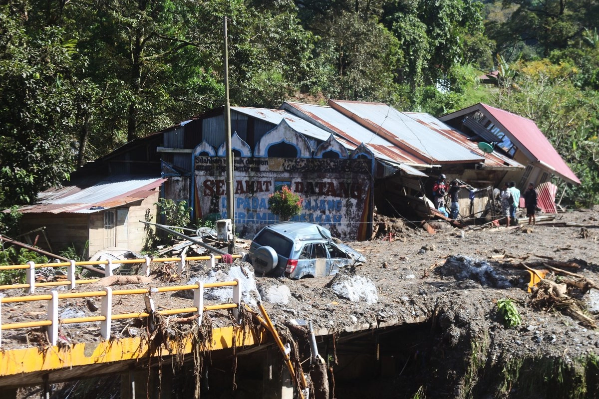 Los restos de un automóvil yacen en medio de una carretera mientras la gente inspecciona los daños tras una inundación repentina en Padang Panjang, Sumatra Occidental, Indonesia, el sábado 29 de noviembre de 2025. Foto