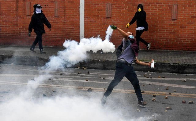Un manifestante lanza un dispositivo de gas lacrimógeno durante choques de activistas con la policía colombiana, durante las protestas contra la reforma fiscal impulsada por el presidente Iván Duque, el 1 de mayo de 2021. Foto Afp