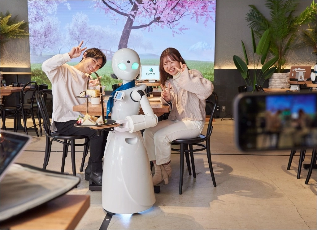 En el café Dawn de la capital japonesa los androides reciben a los clientes, toman pedidos y llevan las tazas a las mesas. Son la cara visible. Detrás están seres humanos, o “pilotos”, que los manejan a distancia con un teléfono o tableta. Es una solución para que personas discapacitadas o que viven fuera del país puedan trabajar. Su creador, Kentaro Yoshifuji, dice que inventó la “teletransportación”. En el segundo año de operación ya es viable económicamente. Foto tomada del sitio web del local 