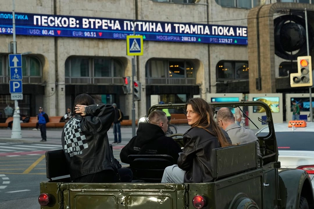 Personas viajan en un vehículo todoterreno soviético GAZ-69 como un teletipo de fondo que informa sobre una posible reunión entre el presidente ruso Vladimir Putin y el presidente estadounidense Donald Trump. Foto