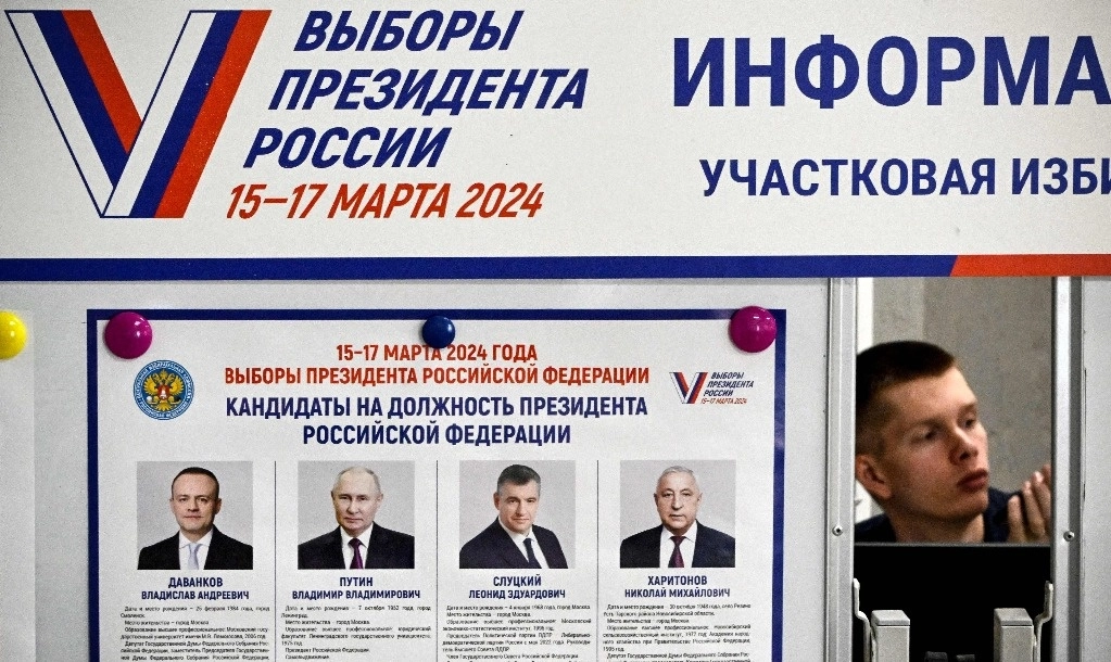 Un miembro de una comisión electoral local se sienta junto a un cartel informativo que muestra a los candidatos de las elecciones presidenciales de Rusia en un colegio electoral en Sergiyev Posad, a unos 75 kilómetros (47 millas) al noreste de Moscú, el 16 de marzo de 2024. Foto Afp