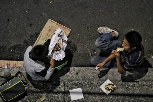 Niños que limpian parabrisas en las calles de la ciudad se dan tiempo para comer sobre el asfalto, durante la cuarentena por el Covid-19 en la Ciudad de México. Foto Marco Peláez / Archivo