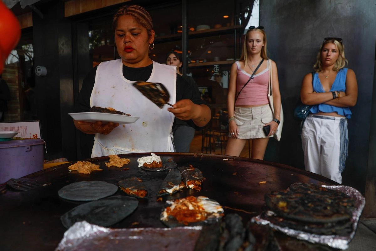 Jennifer Monroy se encarga de llenar el comal de tortillas y voltearlas en el puesto de antojitos mexicanos ‘Elenita’ ante la mirada curiosa de comensales extranjeros. Foto 