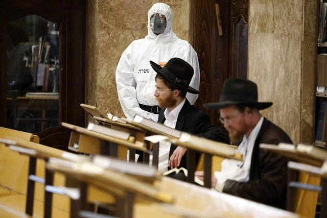 Un policía israelí con traje de protección espera para detener a dos judíos ultraortodoxos por rezar en una sinagoga y desafiar las medidas del gobierno contra el coronavirus. Foto Ap