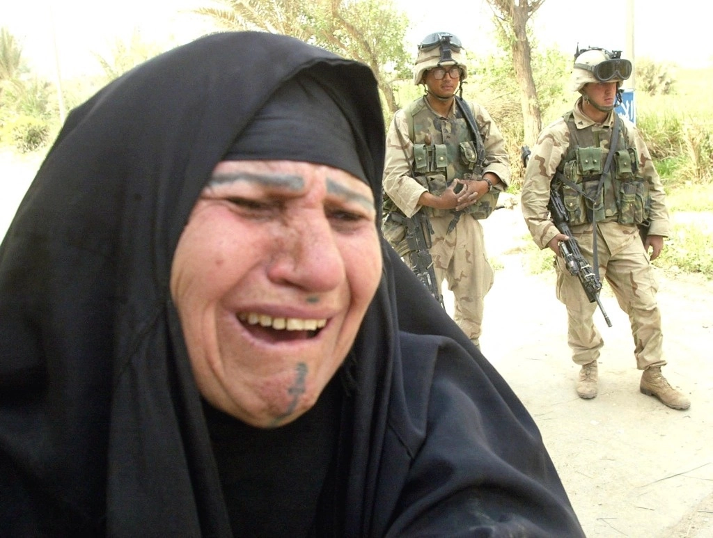 En imagen del 12 de abril de 2003, una mujer iraquí llora porque no puede encontrar a sus dos hijos en el hospital siquiátrico de Bagdad, mientras dos infantes de marina montan guardia en el fondo. A 20 años de la invasión a Irak liderada por Estados Unidos que derrocó a Saddam Hussein, el país rico en petróleo sigue marcado por el conflicto. Foto Afp