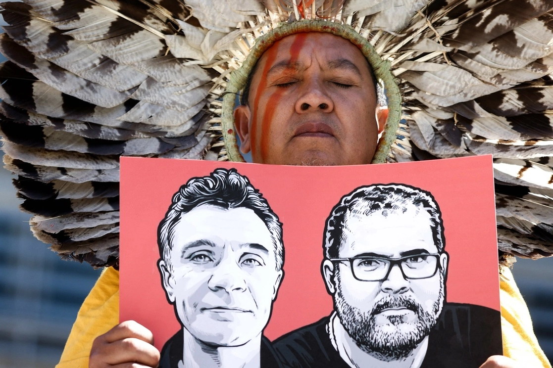 Un miembro de la Articulación de Pueblos Indígenas de Brasil (APIB) sostiene la imagen periodista británico Dom Phillips y el especialista en asuntos indígenas brasileño Bruno Pereira asesinados, durante una manifestación convocada por activistas del grupo de protesta contra el cambio climático Extinction Rebellion (XR). Foto Afp