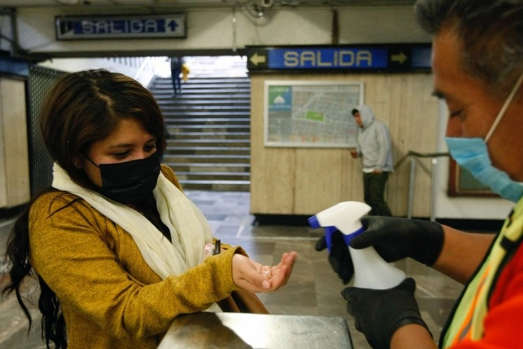 Pasajeros de la Línea 2 del Metro usan tapabocas para prevenir el contagio del Covid-19, mientras un empleado aplica gel antibacterial en los torniquetes. Foto Roberto García Ortiz