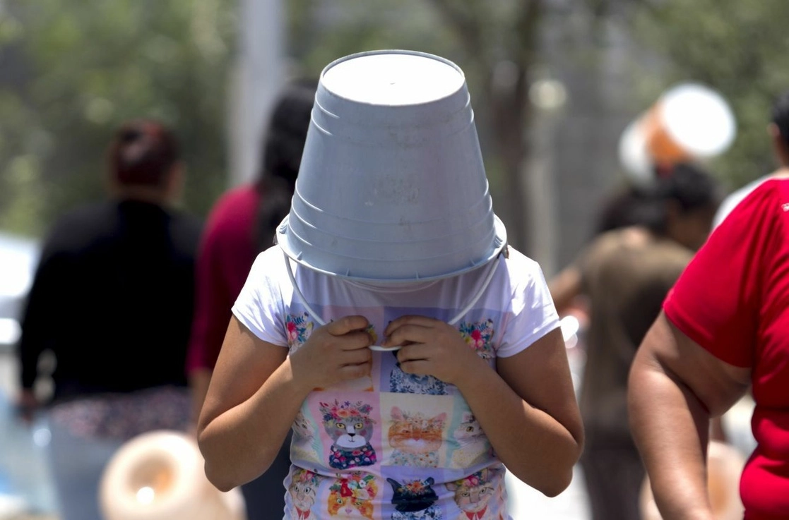 Una mujer cubre su rostro del sol con una cubeta, después de no alcanzar agua de la pipa que llegó a su colonia en el municipio de García, Nuevo León. Foto Cuartoscuro 