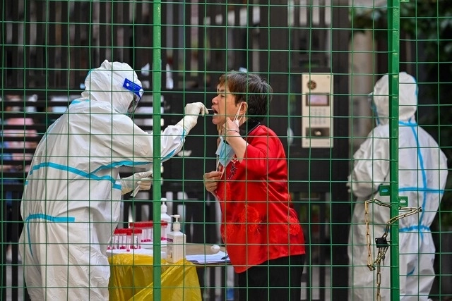 Un trabajador de la salud toma una prueba para detectar coronavirus a una mujer en la entrada de un área residencial, en Shanghai, en imagen de ayer. Foto Afp 