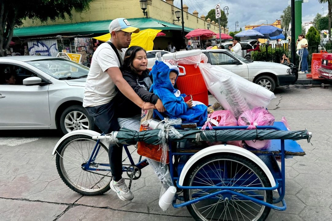 Un padre traslada a su familia en triciclo tras terminar su jornada vendiendo café, pan y tamales, en el Día del Padre.